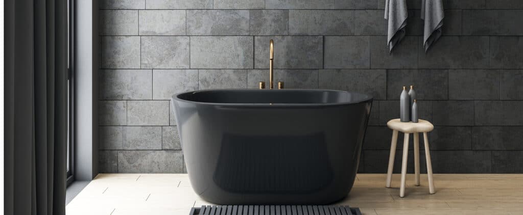 Baignoire îlot noire moderne dans salle de bain minimaliste, murs en carrelage ardoise sombre et robinetterie laiton.