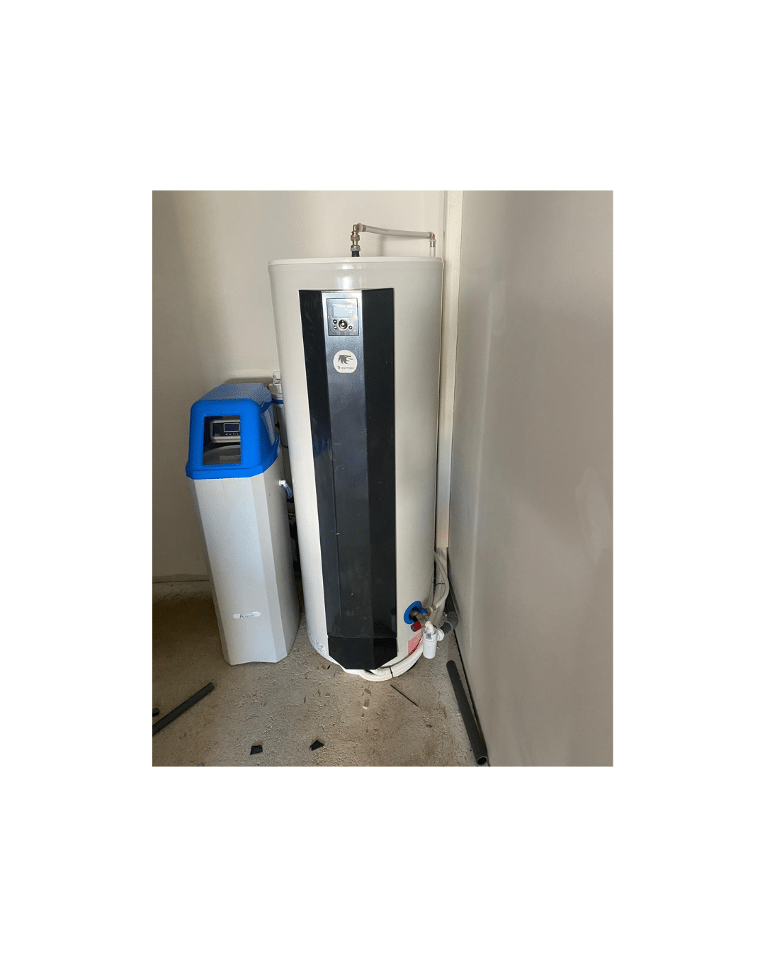 Chauffe-eau thermodynamique blanc et noir avec affichage digital, à côté d'un adoucisseur d'eau bleu et blanc dans une pièce de service.