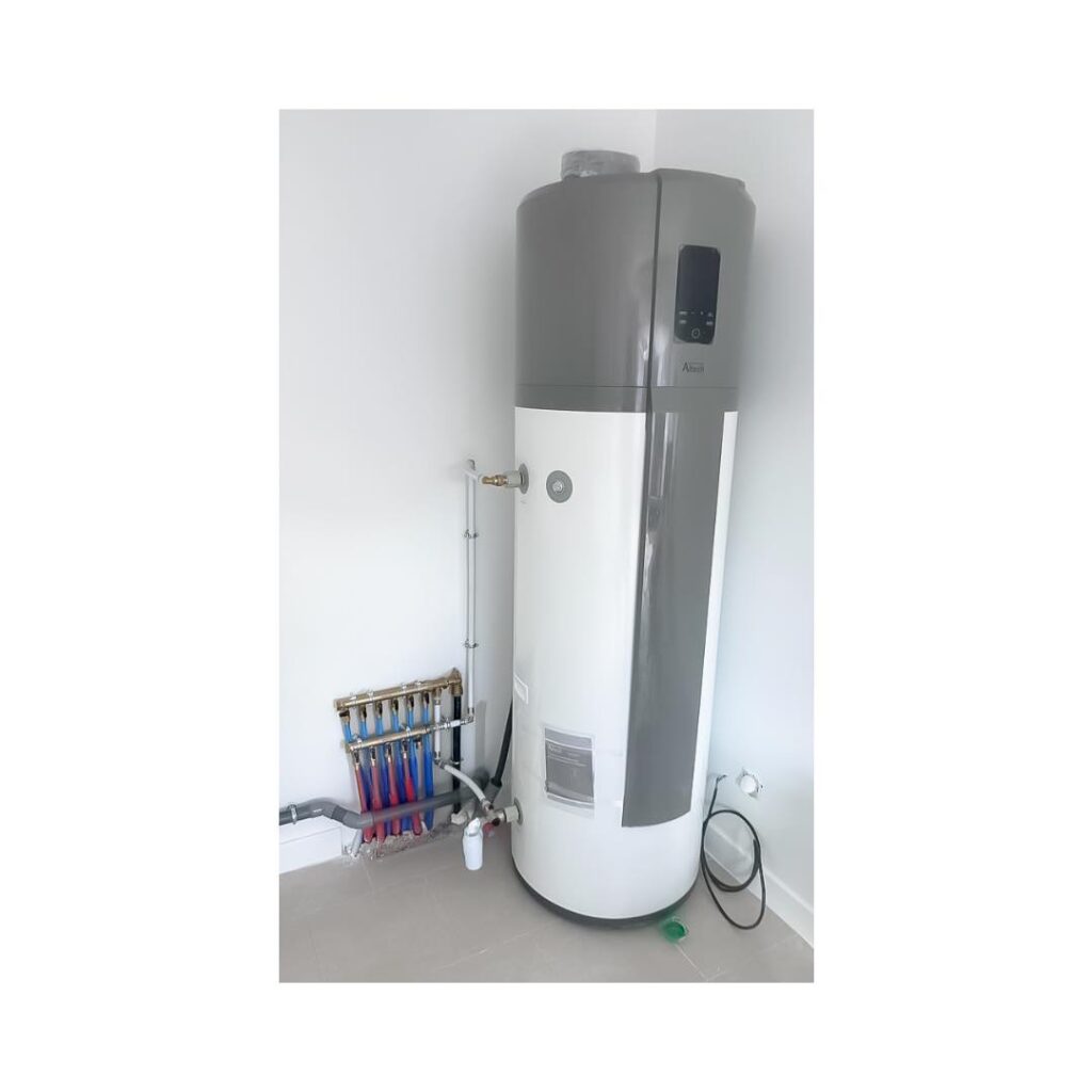 Chauffe-eau Thermodynamique Aira et Collecteur Chauffage Ballon d'eau chaude thermodynamique blanc et gris avec panneau de contrôle affichant 'Aira', près d'un collecteur de chauffage au sol avec tuyaux rouges et bleus.