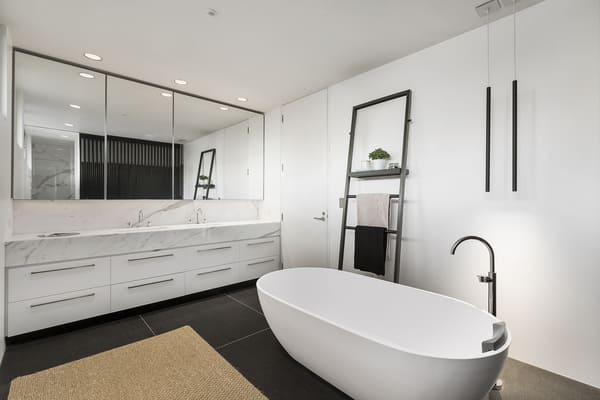 Salle de bain moderne épurée avec grande vanité en marbre, baignoire îlot blanche et accents noirs, éclairage minimaliste.
