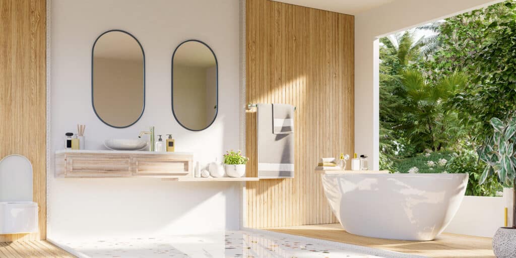 Salle de bain moderne avec murs blancs, bois clair, deux miroirs ovales, lavabo sur meuble flottant et baignoire face à la végétation luxuriante.