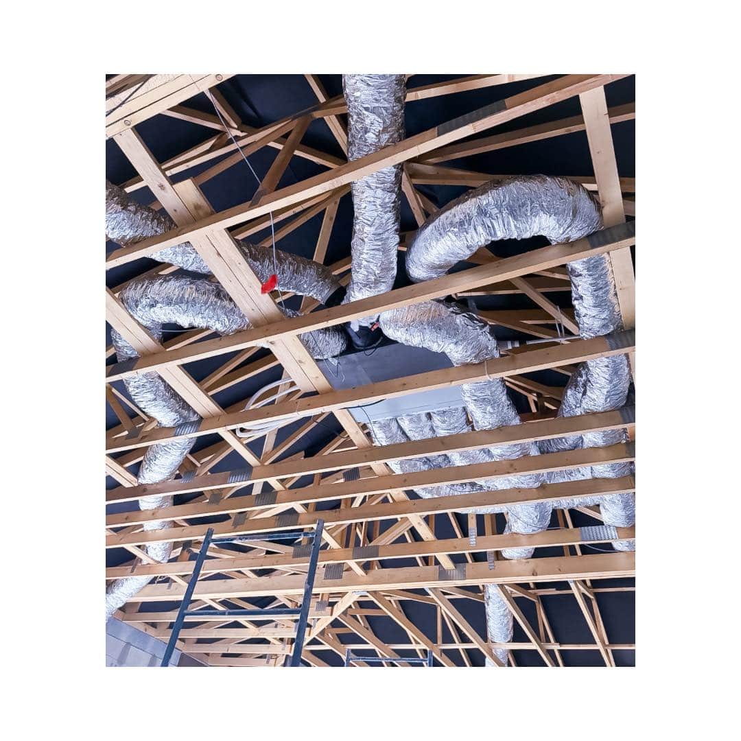 Structure de charpente en bois avec conduits de ventilation isolés et un caisson de traitement d'air installés dans un grenier ou espace sous toit.